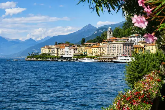 Bellagio nad jeziorem Como z zabudową przy brzegu, górami i kwiatami na pierwszym planie