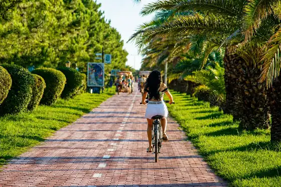 Bulwar w Batumi w Adżarii: rowerzystka jedzie ceglanym deptakiem wśród palm i zieleni.