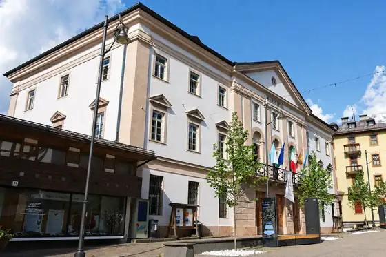 Cortina d'Ampezzo, budynek ratusza przy placu z flagami i drzewami