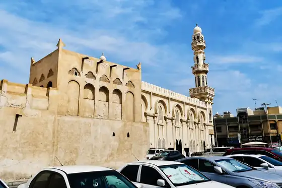 Dom szejka Isy bin Alego w Muharrak z fasadą, minaretem i zaparkowanymi samochodami
