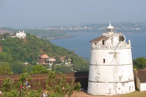 Fort Aguada w Candolim z białą latarnią nad zatoką i wzgórzem w tle