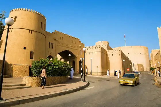 Fort Nizwa i suk w Omanie, przy ulicy z murem i wieżami twierdzy.