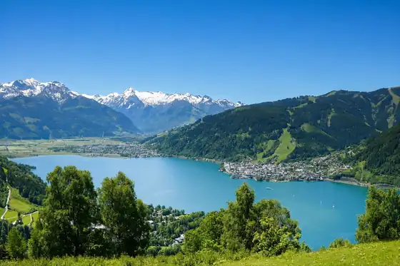 Jezioro Zell i promenada Zell am See widoczne z zielonego stoku z górami w tle.