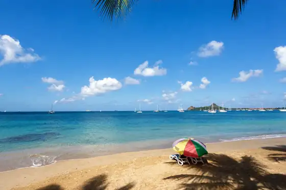 Marina i plaża w Rodney Bay na tle zatoki, żaglówki na wodzie i parasol na piasku.