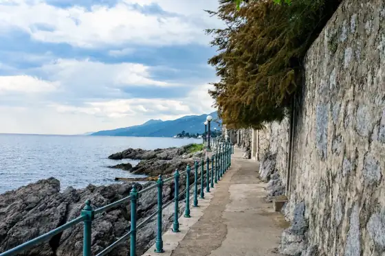Opatija i promenada Lungomare wzdłuż skalistego brzegu, z balustradą i murem.