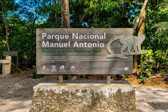 Tablica Parku Narodowego Manuel Antonio w Quepos, otoczona tropikalną roślinnością.