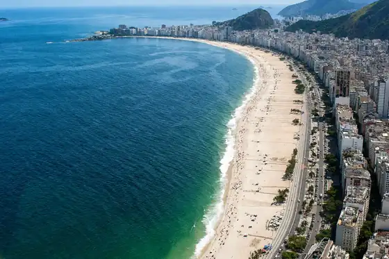 Plaża Copacabana w Rio de Janeiro z łukiem brzegu, morzem i zabudową przy plaży.