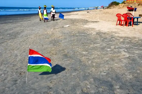 Plaża Kotu i Kololi w Kololi: piasek, flaga i ludzie idący przy brzegu.
