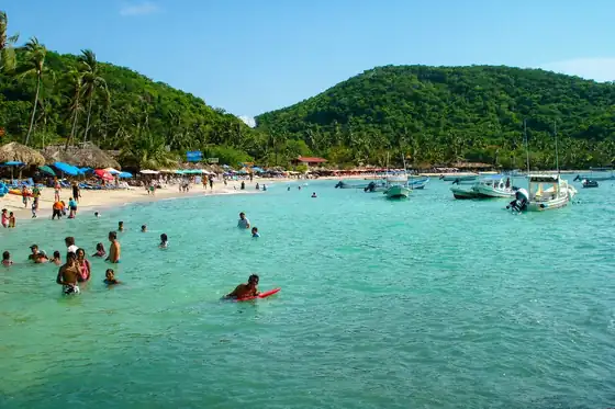 Plaża Las Gatas w Zihuatanejo z kąpiącymi się ludźmi i łodziami przy brzegu.
