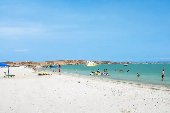 Plaża Playa La Punta na Coche z białym piaskiem, ludźmi w wodzie i łodzią na morzu.