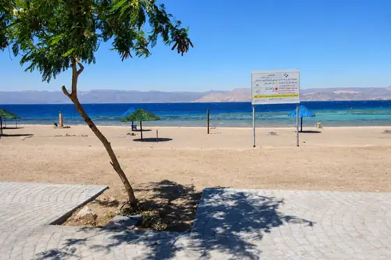 Plaża Południowa w Akabie z piaszczystym brzegiem, morzem i tablicą przy zejściu na plażę.
