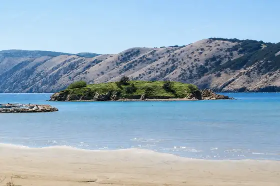 Plaża Rajska w Loparze z piaszczystym brzegiem, spokojnym morzem i wysepką na tle wzgórz