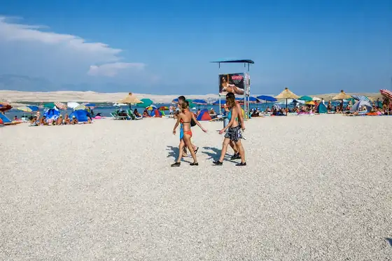 Plaża Zrće w Novalji z ludźmi na żwirowym brzegu, parasolami i morzem w tle.