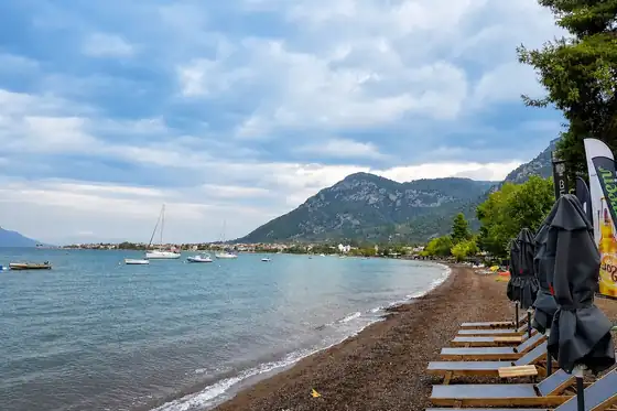 Plaże Kamena Vourla w Grecji Środkowej z leżakami, łodziami i górami nad brzegiem