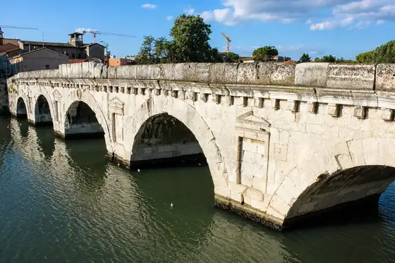 Most Tyberiusza w Rimini nad wodą, z łukami i zabudową w tle