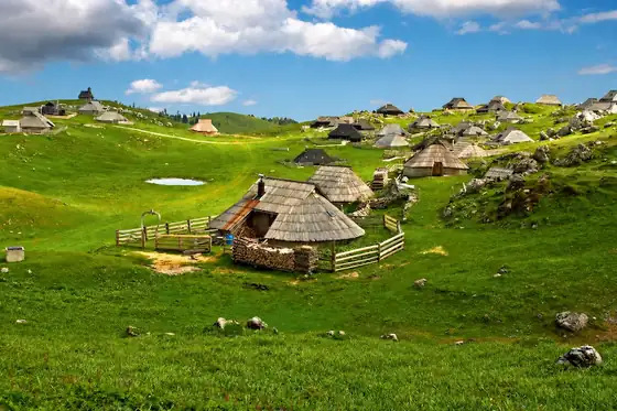 Velika Planina w Kamniku: łąki z drewnianymi szałasami i zagrodami na wzgórzach