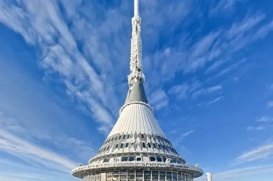 Wieża Ještěd w Libercu na tle błękitnego nieba z rozproszonymi chmurami.