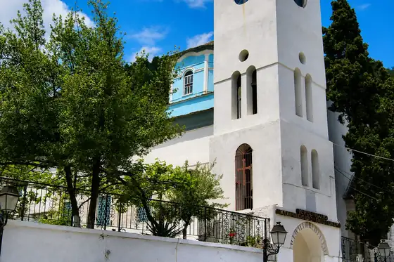 Wioska Panagia w Grecji, biały kościół z wieżą i niebieską kopułą wśród drzew