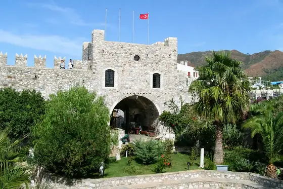 Zamek i stare miasto w Marmaris z kamienną bramą, zielenią i flagą Turcji.