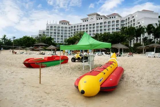 Zatoka Yalong w Sanya z plażą, sprzętem wodnym i dużym hotelem w tle
