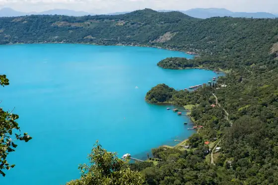 Jezioro Coatepeque w Salwadorze otoczone jest zielonymi wzgórzami i brzegiem z pomostami.