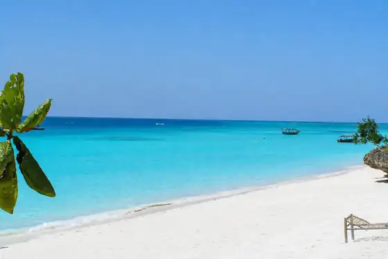 Plaża Nungwi na Zanzibarze w Tanzanii z białym piaskiem, turkusową wodą i łodziami na horyzoncie