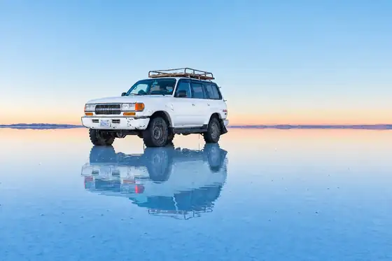 Samochód stoi na tafli Salar de Uyuni w Boliwii.