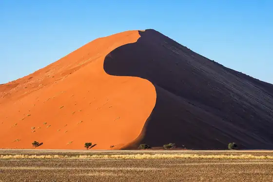 Wydmy Sossusvlei w Namibii z pomarańczowym zboczem i ciemnym cieniem pod niebem.